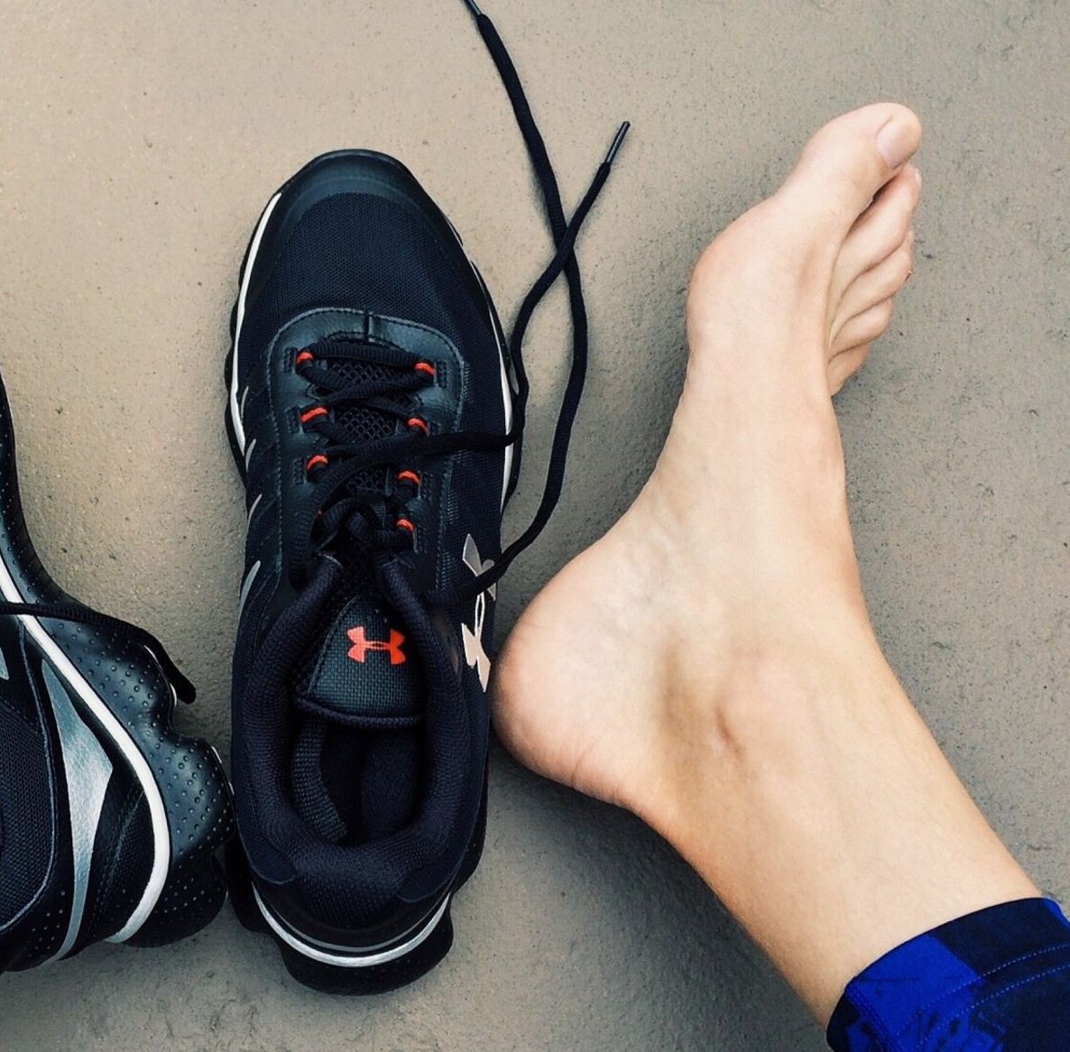 A person 's foot next to a pair of under armour shoes