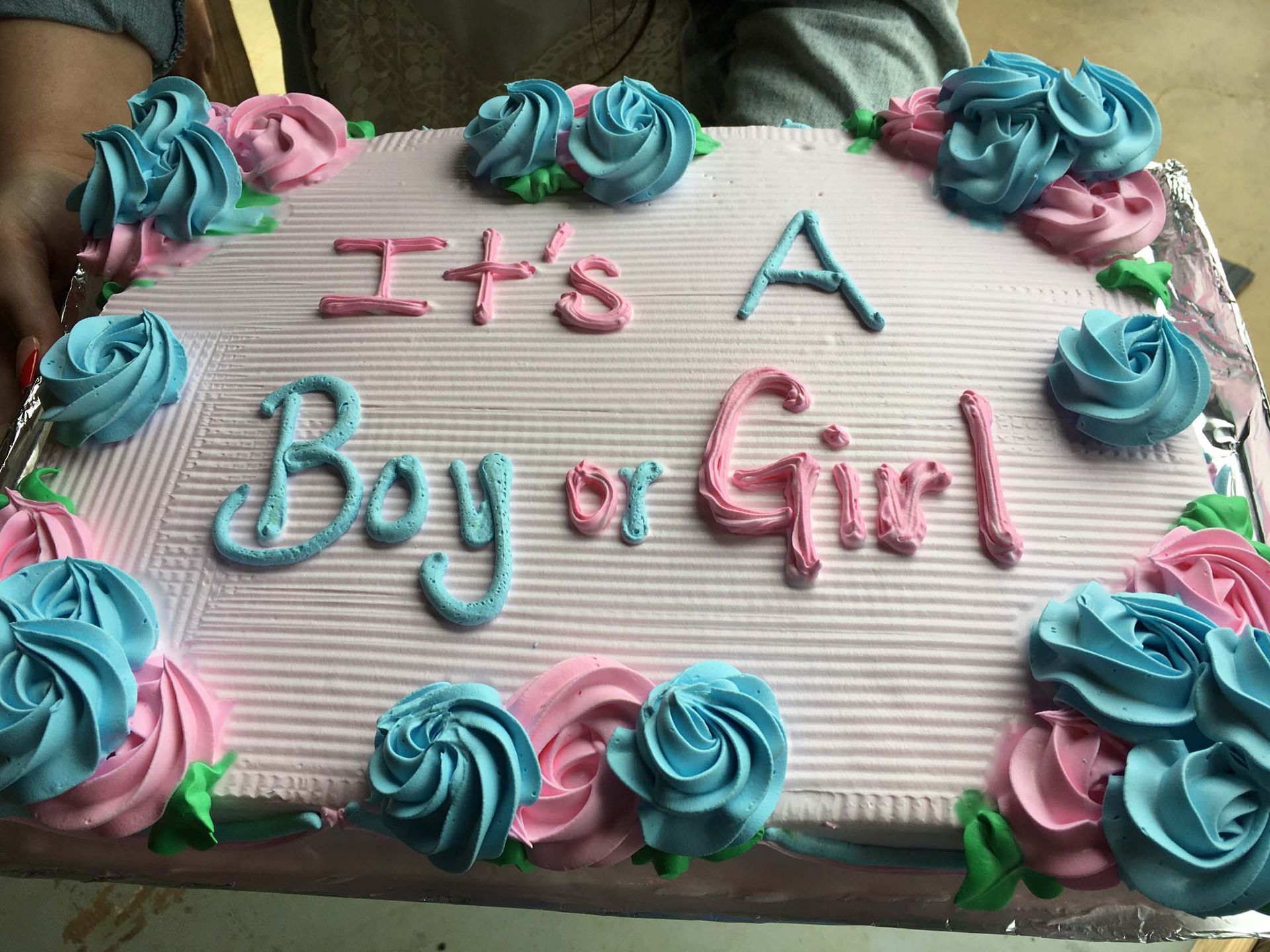 Pink cake with blue and pink frosting rosettes reads “It’s A Boy or Girl”
