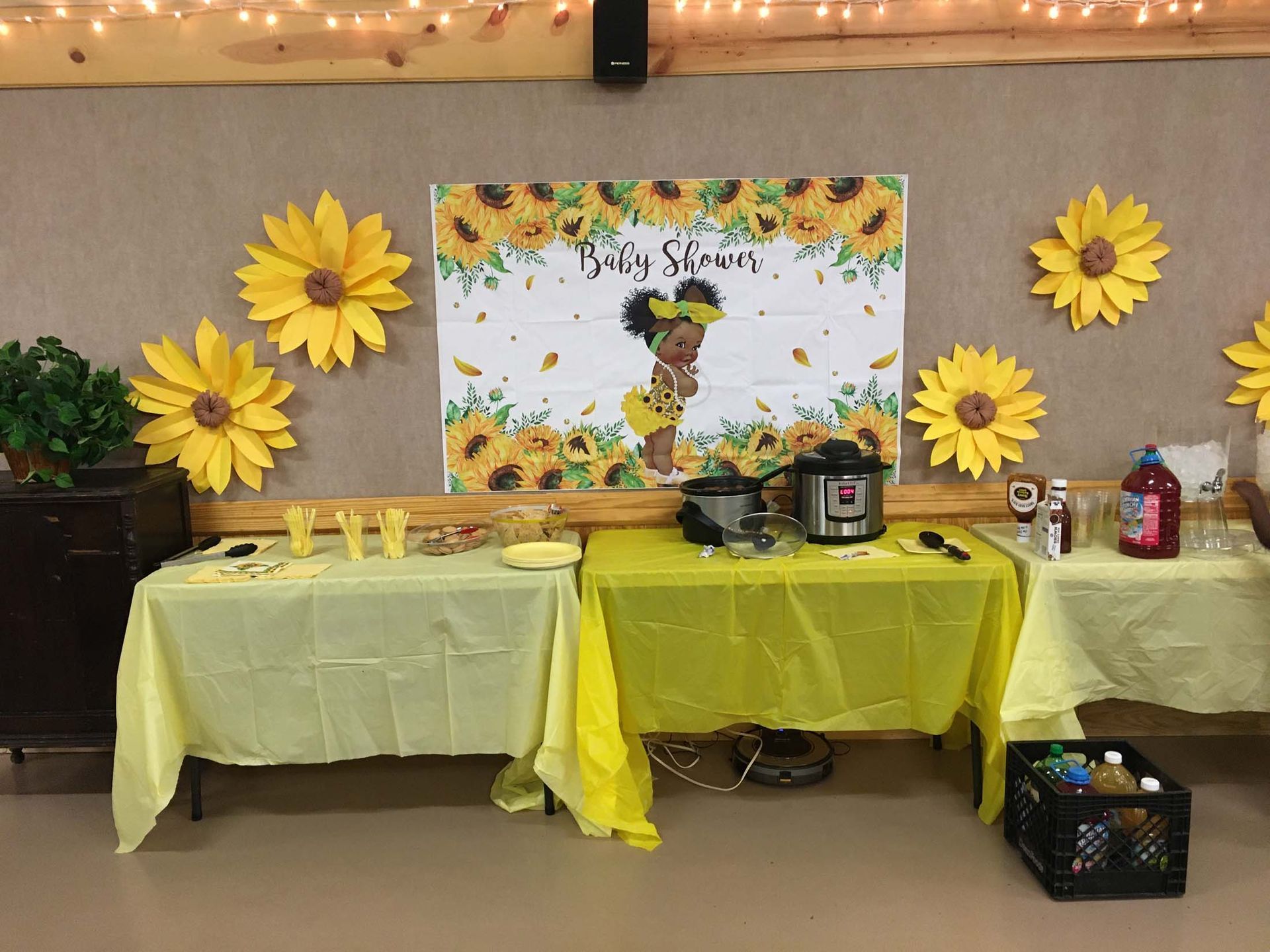 Baby shower dessert table with yellow decor, flowers, banner, and drinks on a beige wall backdrop