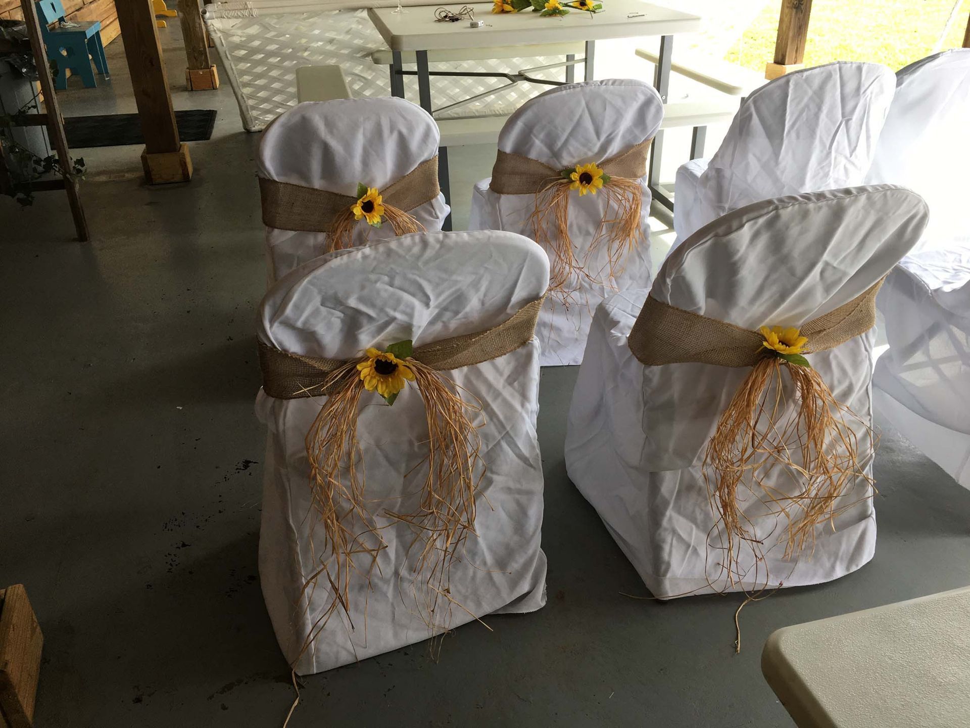 Five white chair covers tied with burlap and yellow flowers in a decorated indoor venue