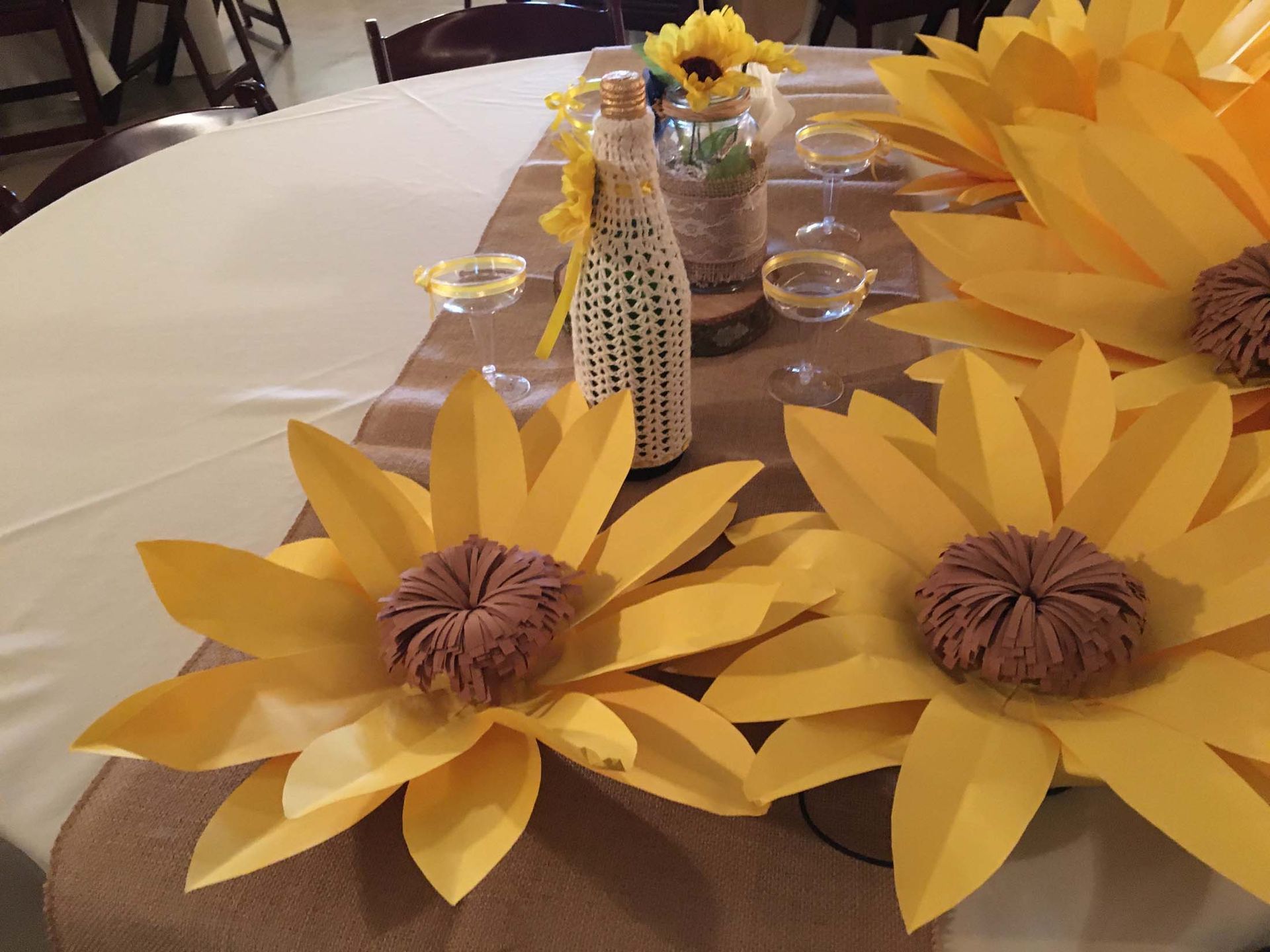 Sunflower paper centerpieces on a white table with yellow decorations and small vases