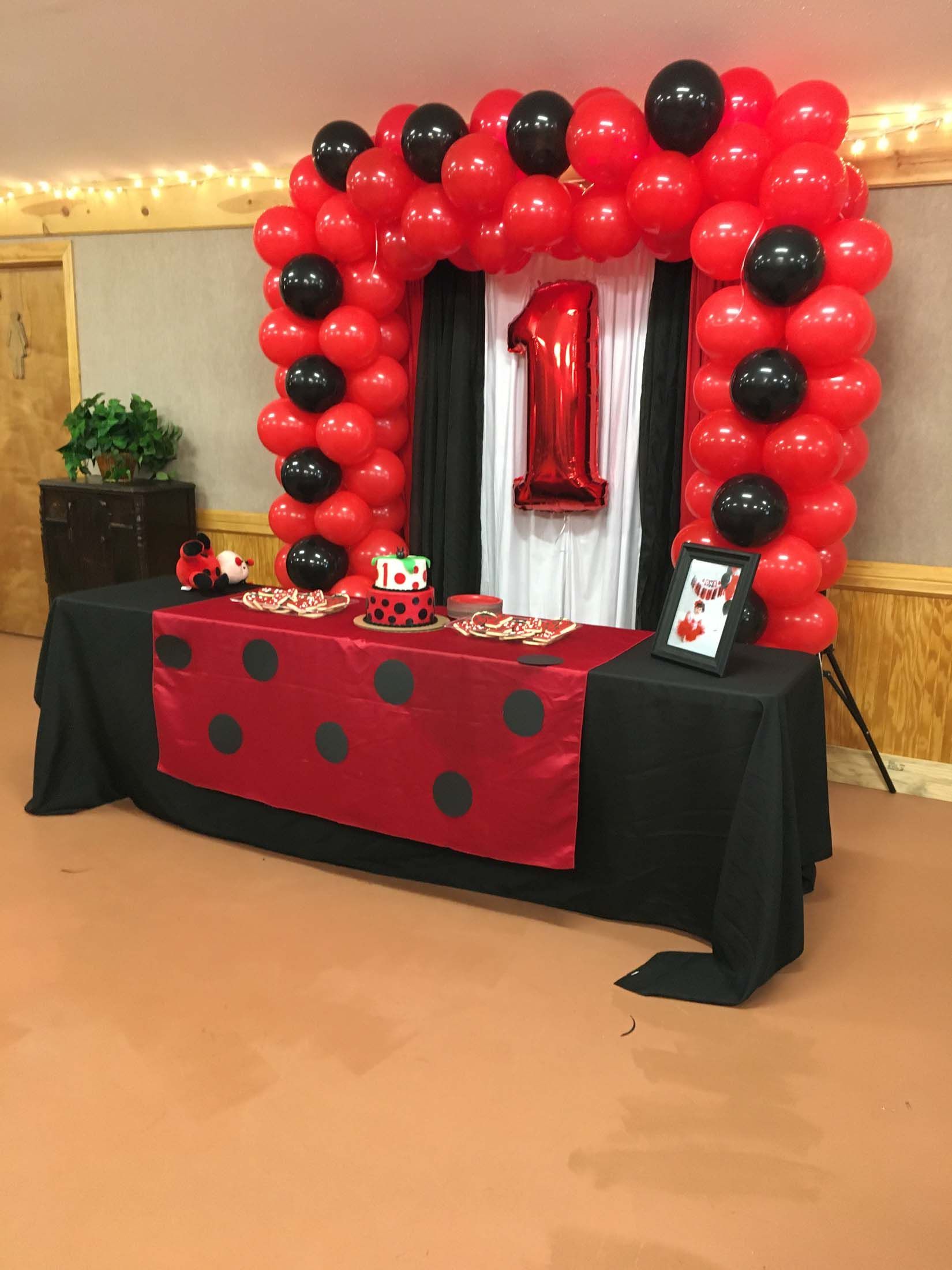 Red and black balloon arch over a decorated table at an indoor party display