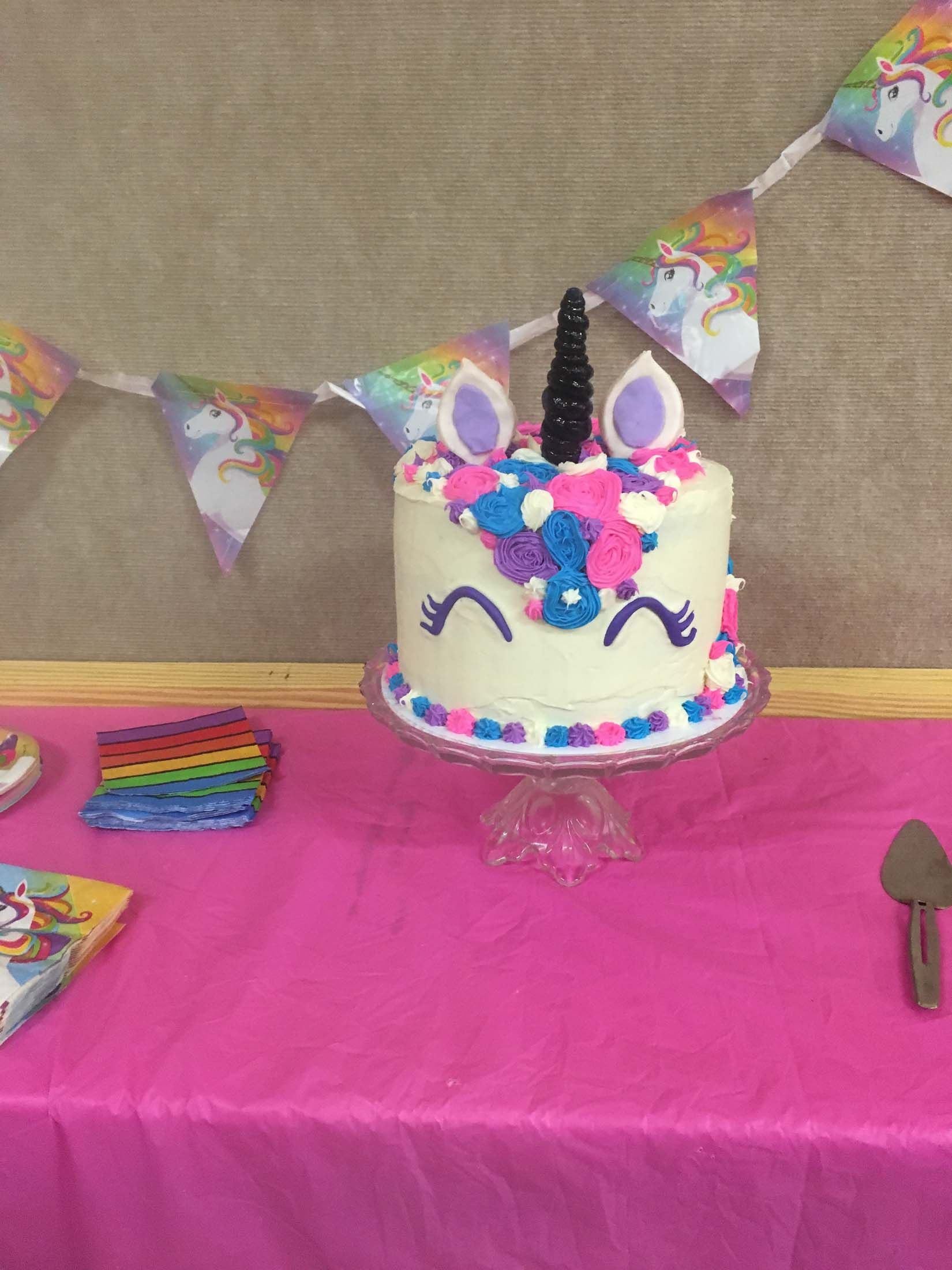 Decorated unicorn birthday cake on a pink-covered table with bunting in the background
