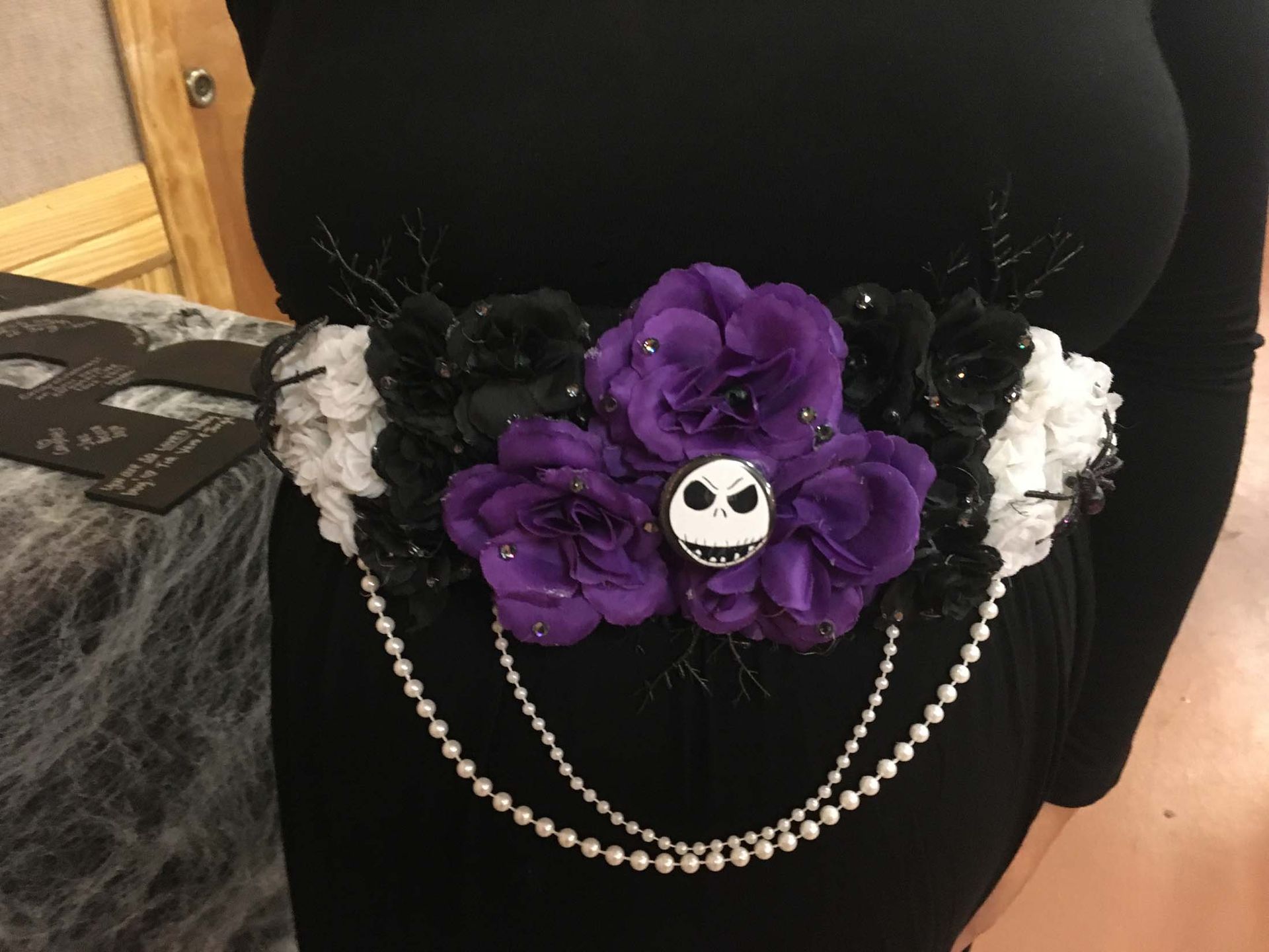 Black belt with purple flowers, skull charm, and pearl chains on a black dress