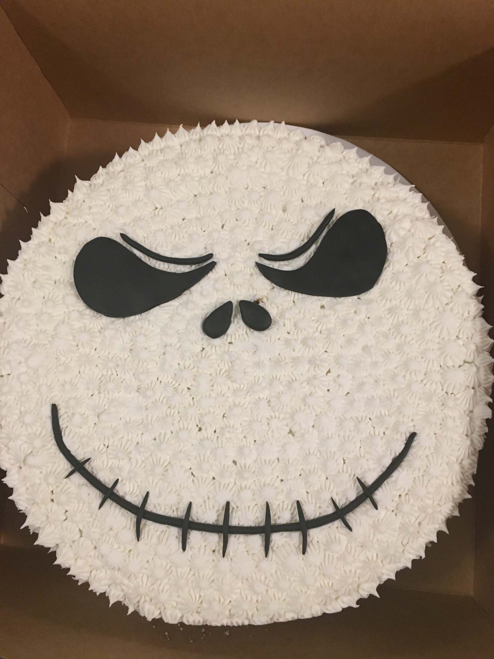 White round Jack Skellington cake with black eyes and stitched smile in a box