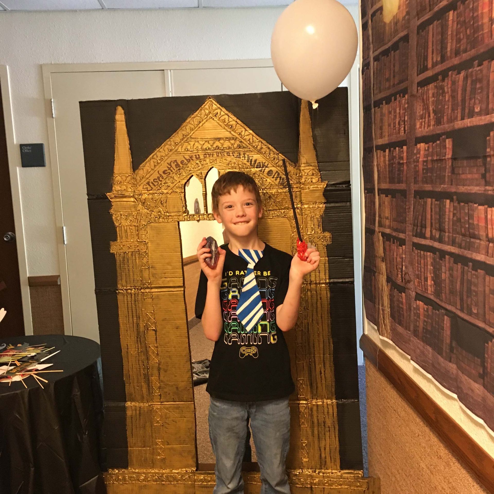 Child posing in front of a cardboard castle display, holding a balloon and smiling