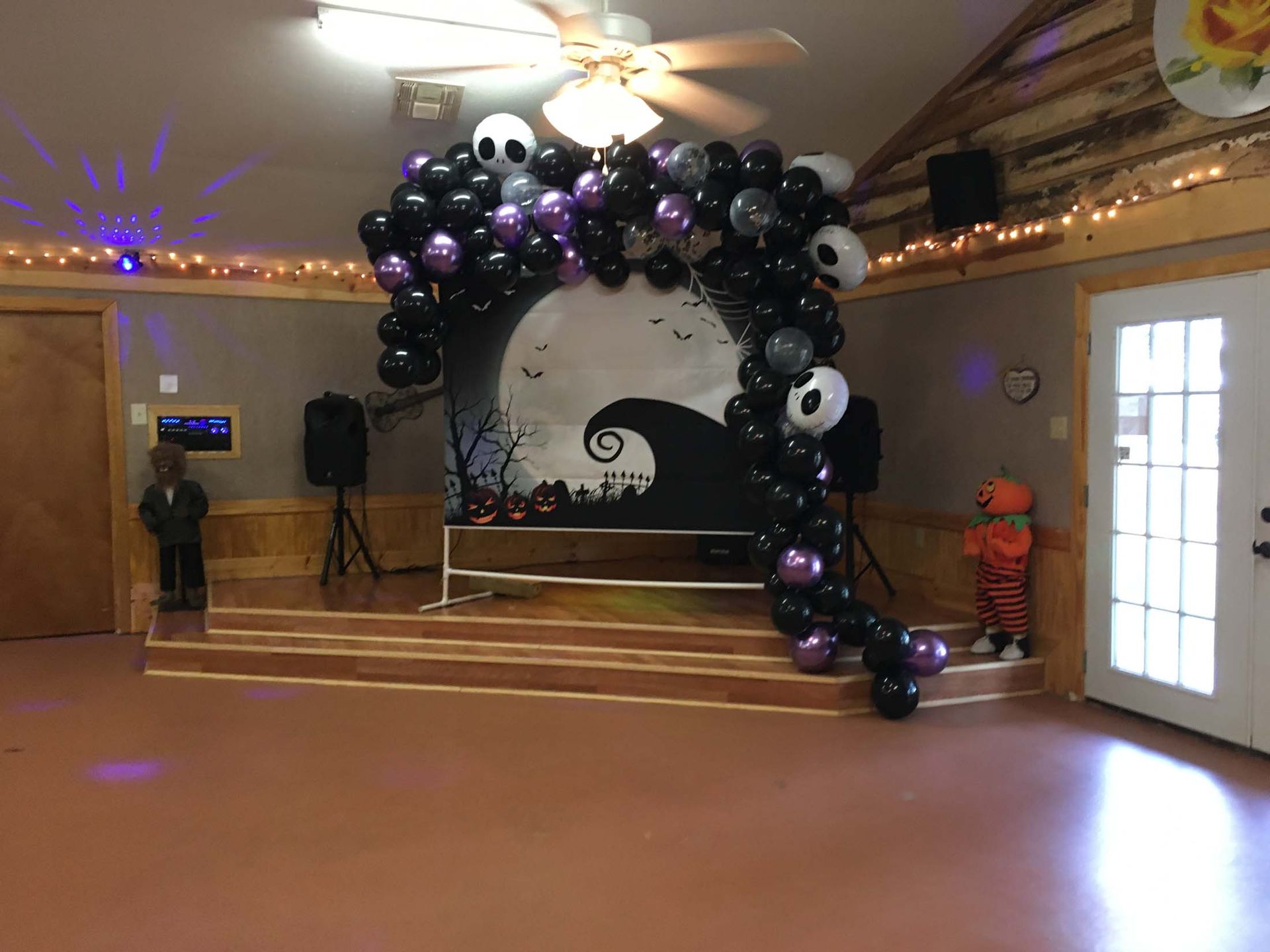 Balloon arch backdrop with black, white, and purple balloons on a small indoor stage at an event hall.