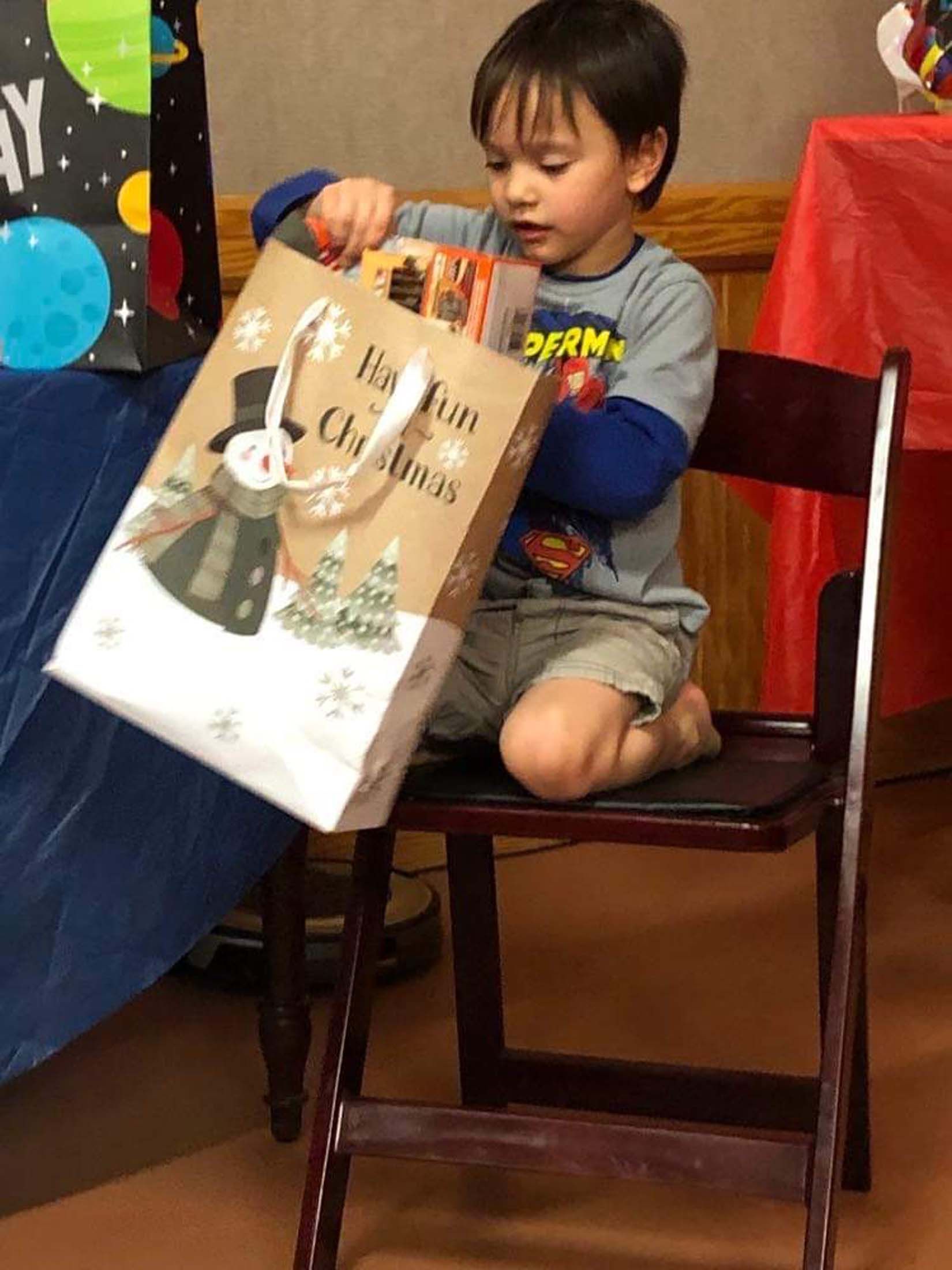 Child opening a gift bag while sitting on a chair at a colorful birthday party table