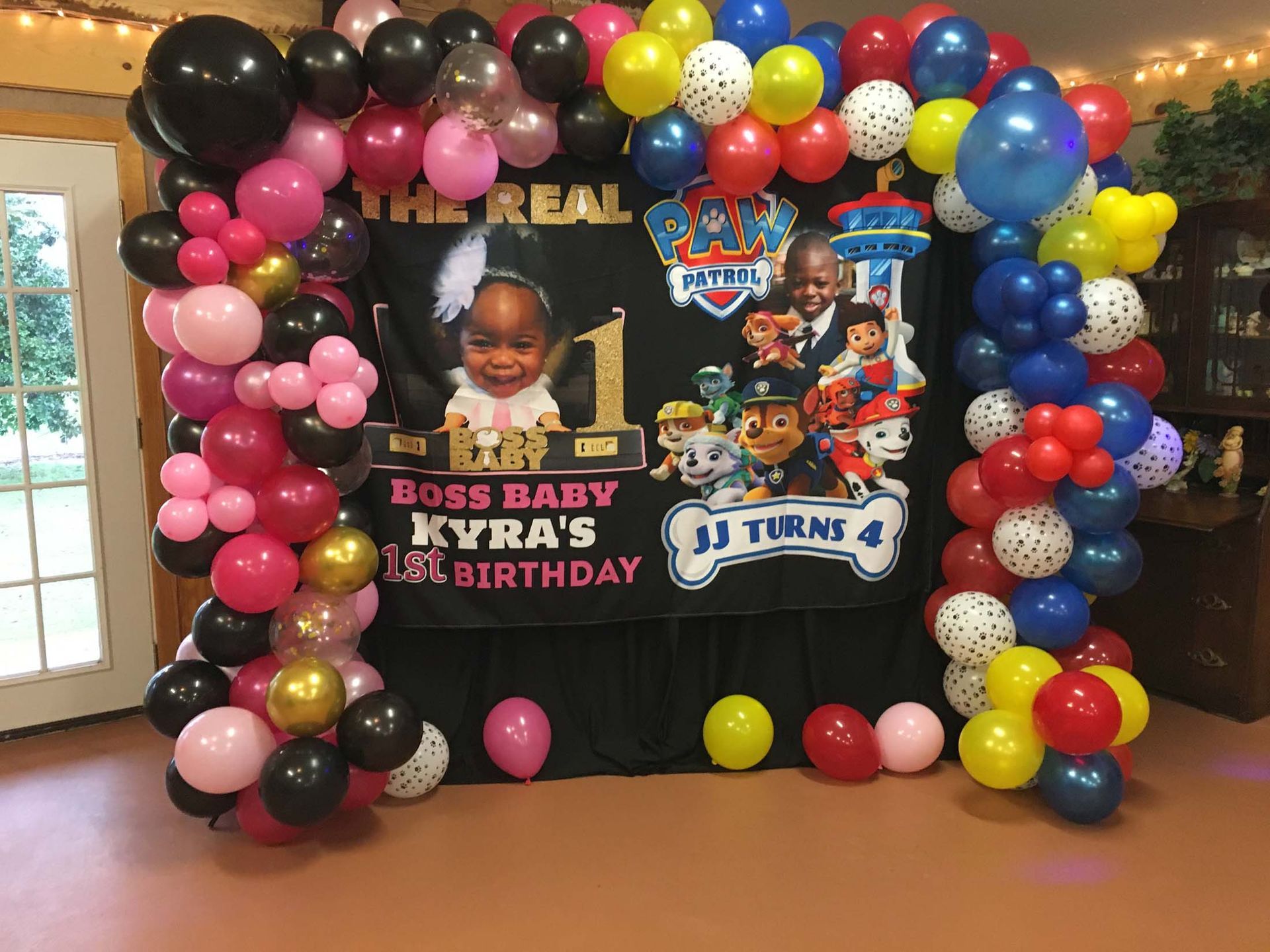 Birthday photo backdrop with colorful balloon arch, child photos, and “1st birthday” decorations