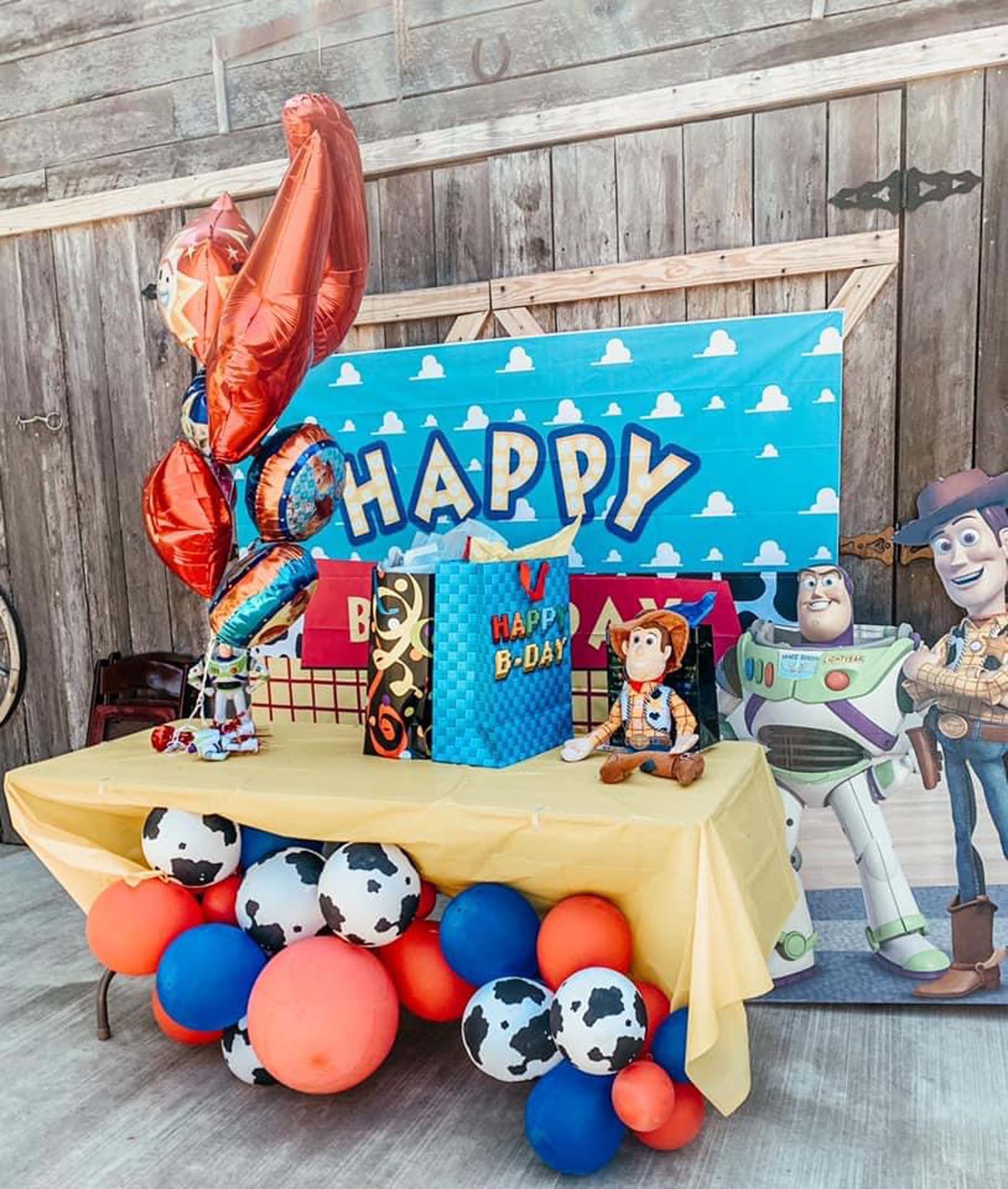 Toy Story birthday table with balloon decorations, a “HAPPY” banner, and character cutouts