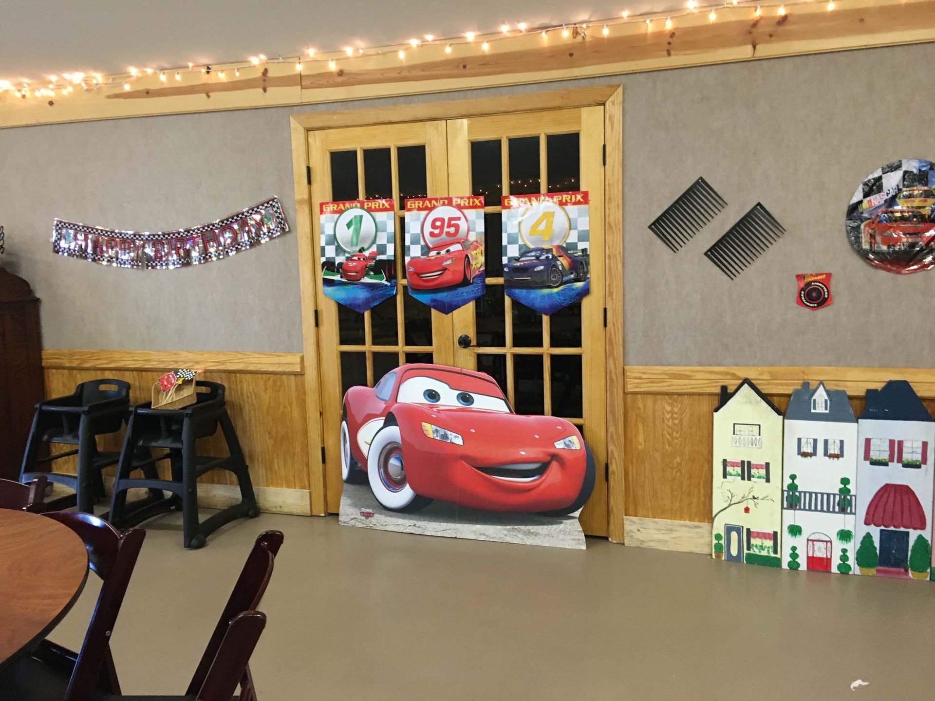 Cars-themed party room with a cardboard Lightning McQueen cutout and red-and-blue decorations on the wall.
