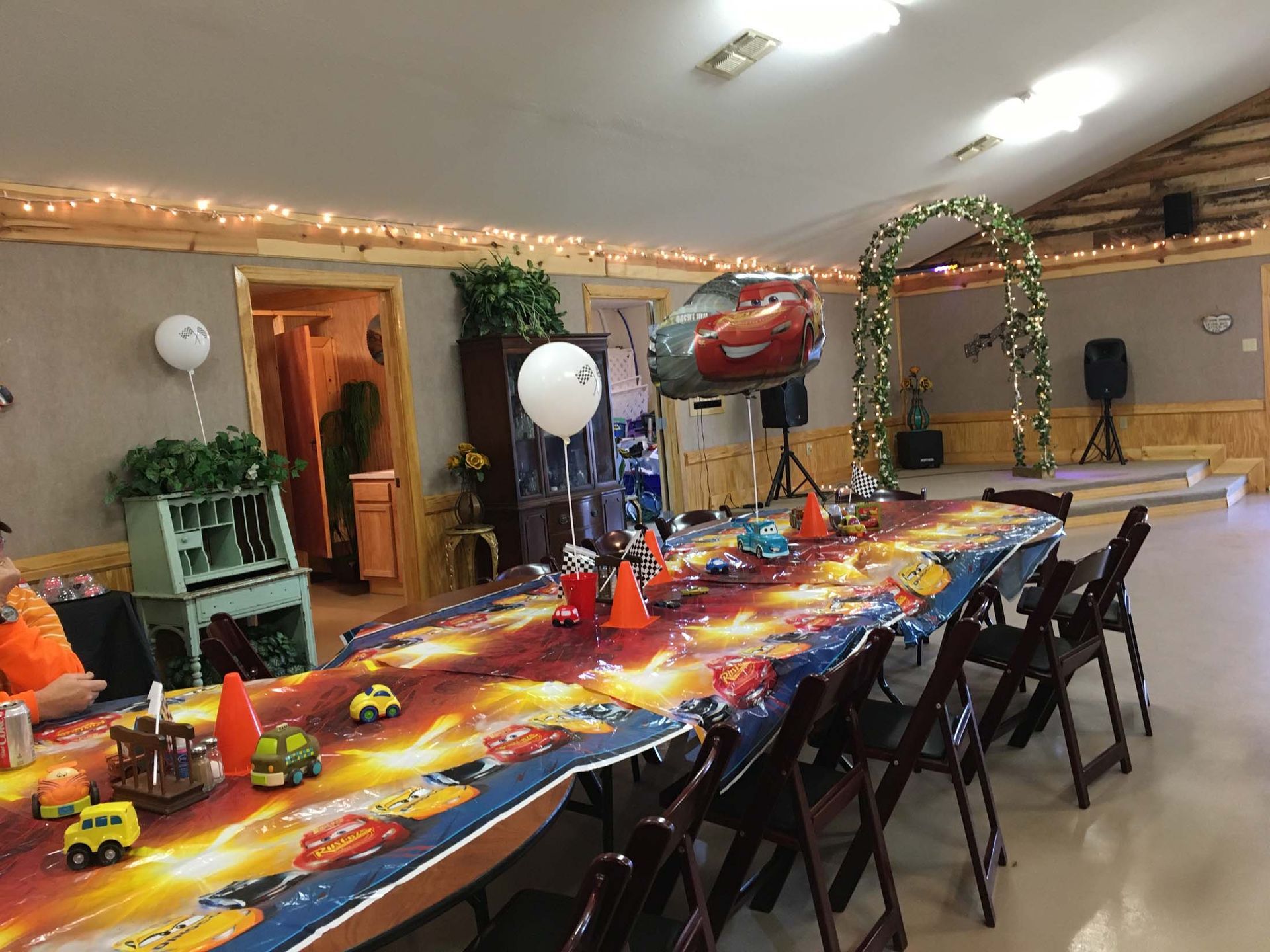 Party table with colorful space-themed tablecloth, balloons, and decorations in a hall
