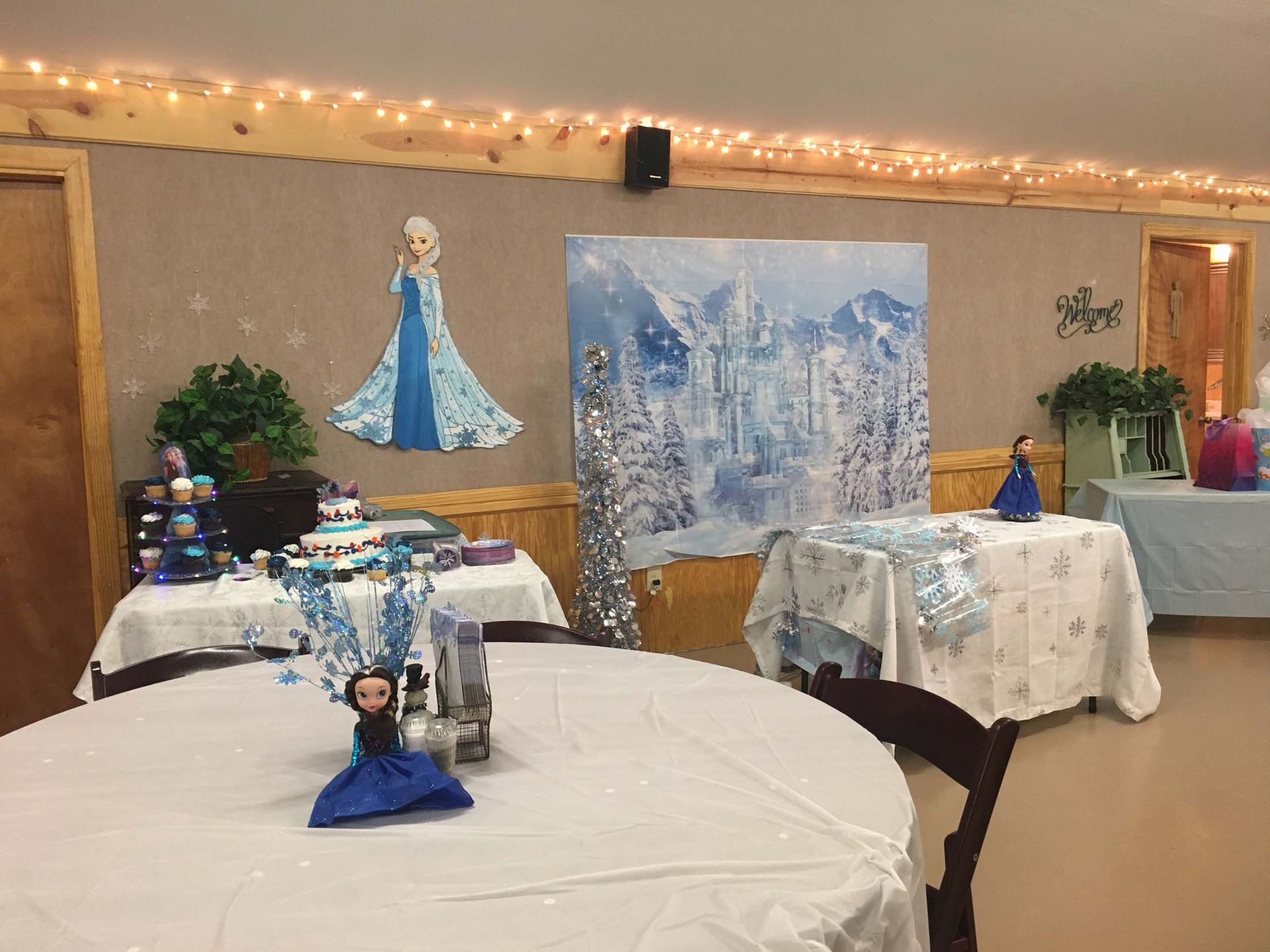 Decorated banquet room with frozen-themed tables, a princess cutout, and blue-white party decor