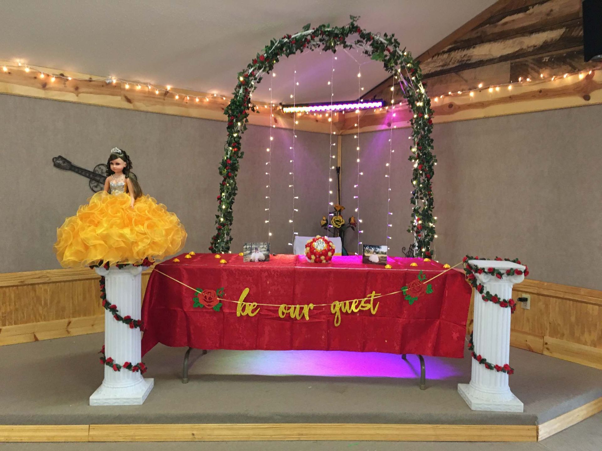 Decorated table setup with floral arch, string lights, and a yellow dress display on the left.
