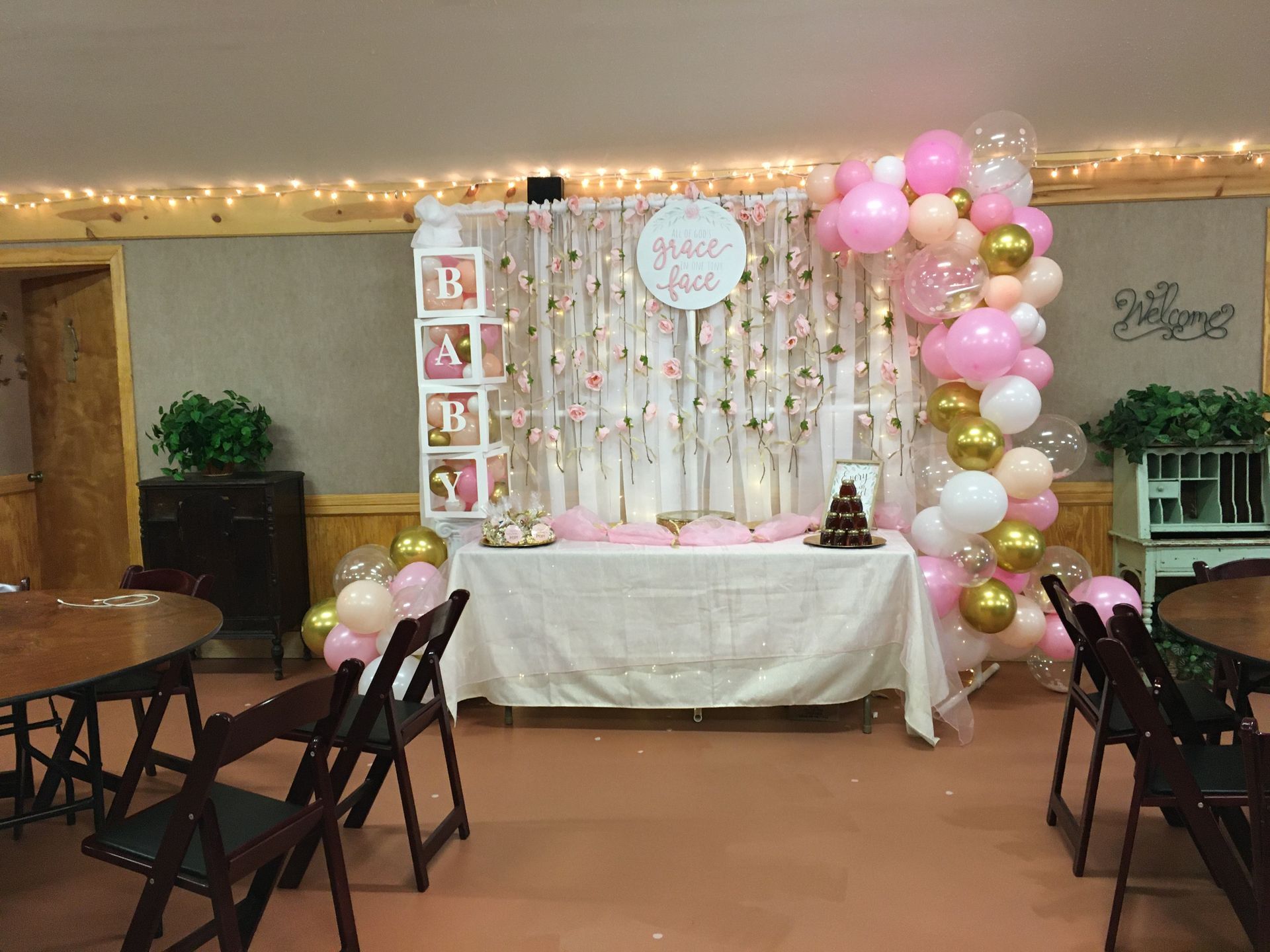 Decorated party dessert table with pink balloons, a cake, and framed photos against a white backdrop