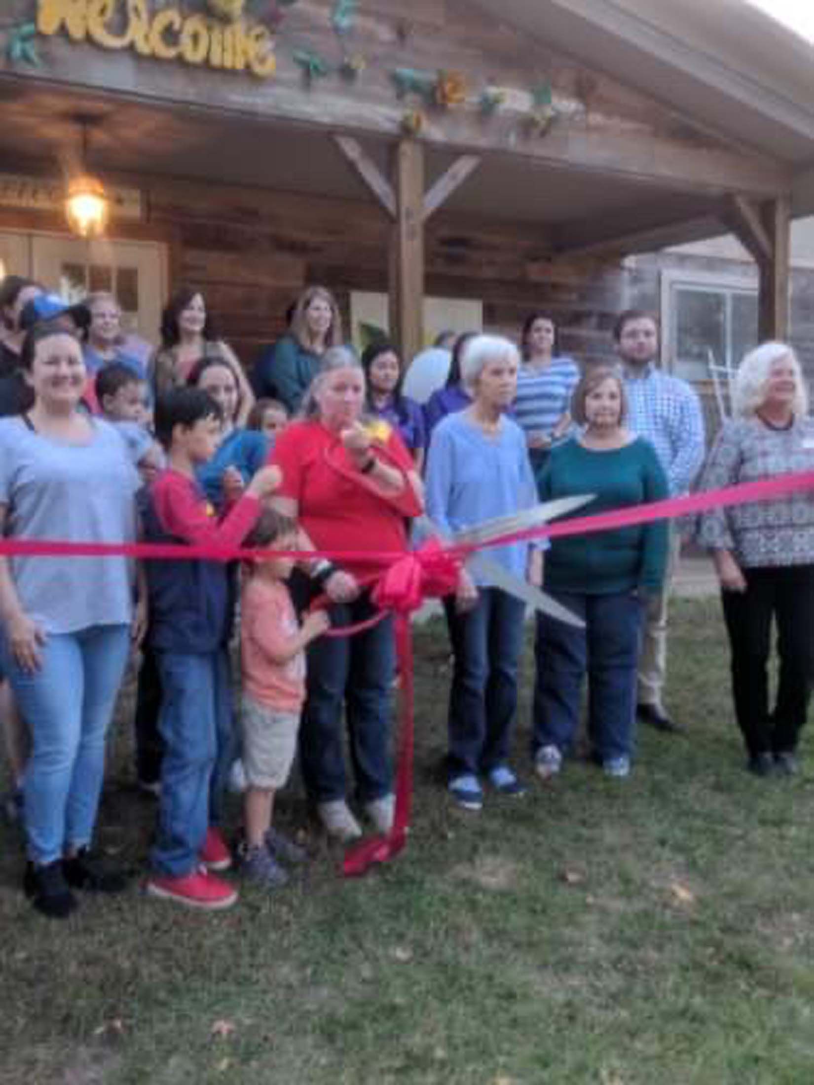 Group gathered outside a wooden building at a red ribbon cutting ceremony.