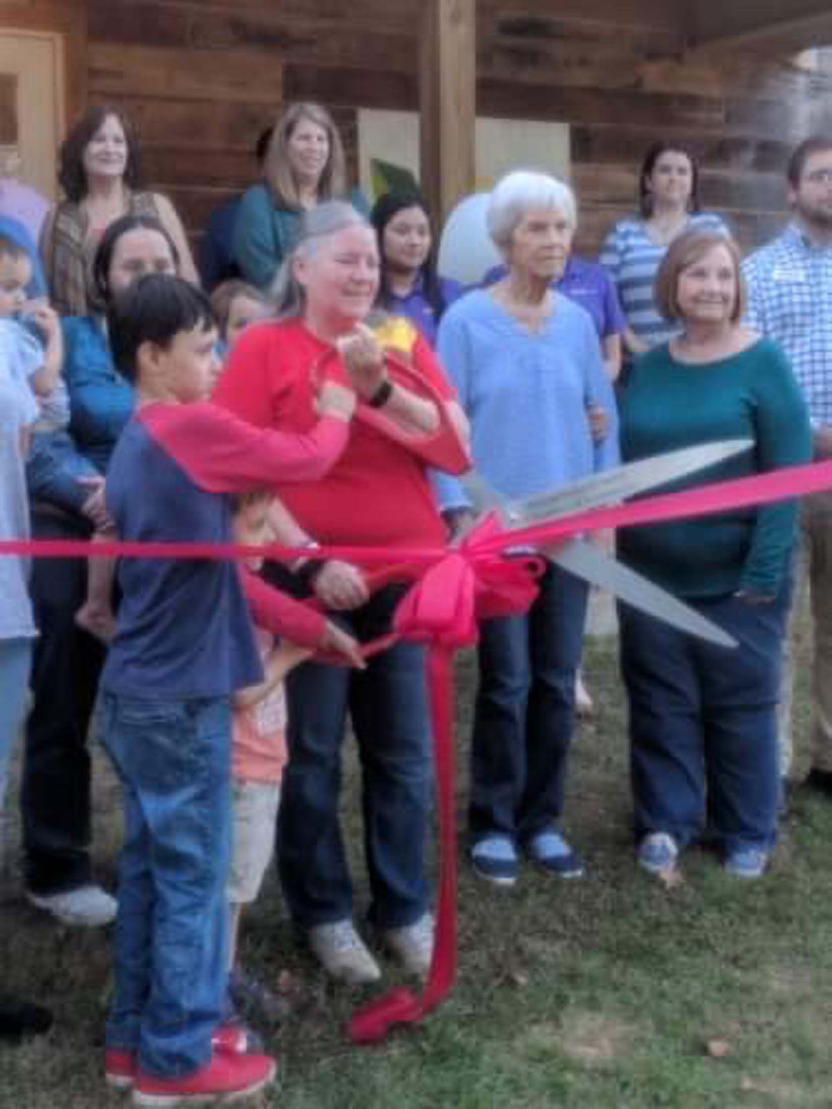People gathered at a ribbon-cutting ceremony outside a wooden building.