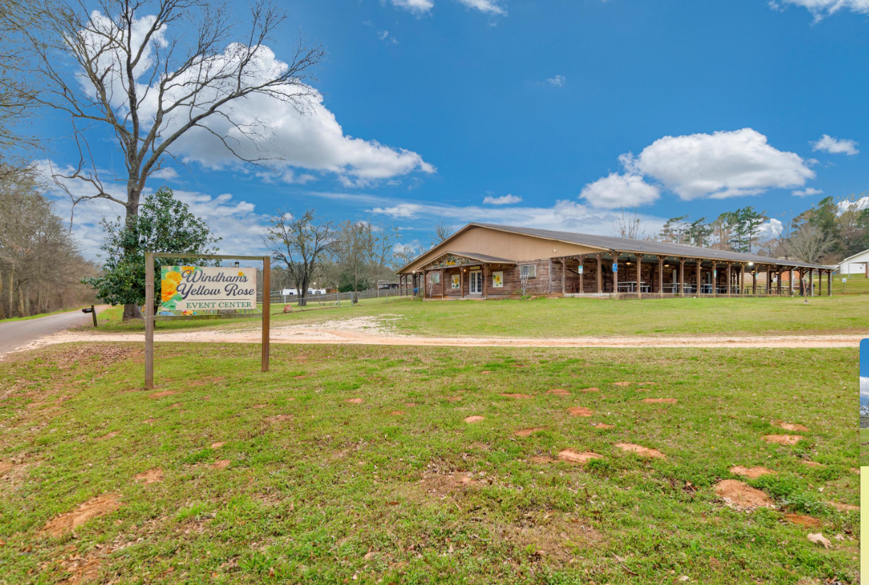 Rural building with porch beside a grassy field under a blue sky, with a sign in the foreground