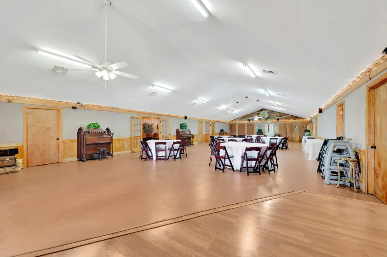 Spacious hall with round tables and chairs under bright ceiling lights, wood-paneled walls, and polished floor.