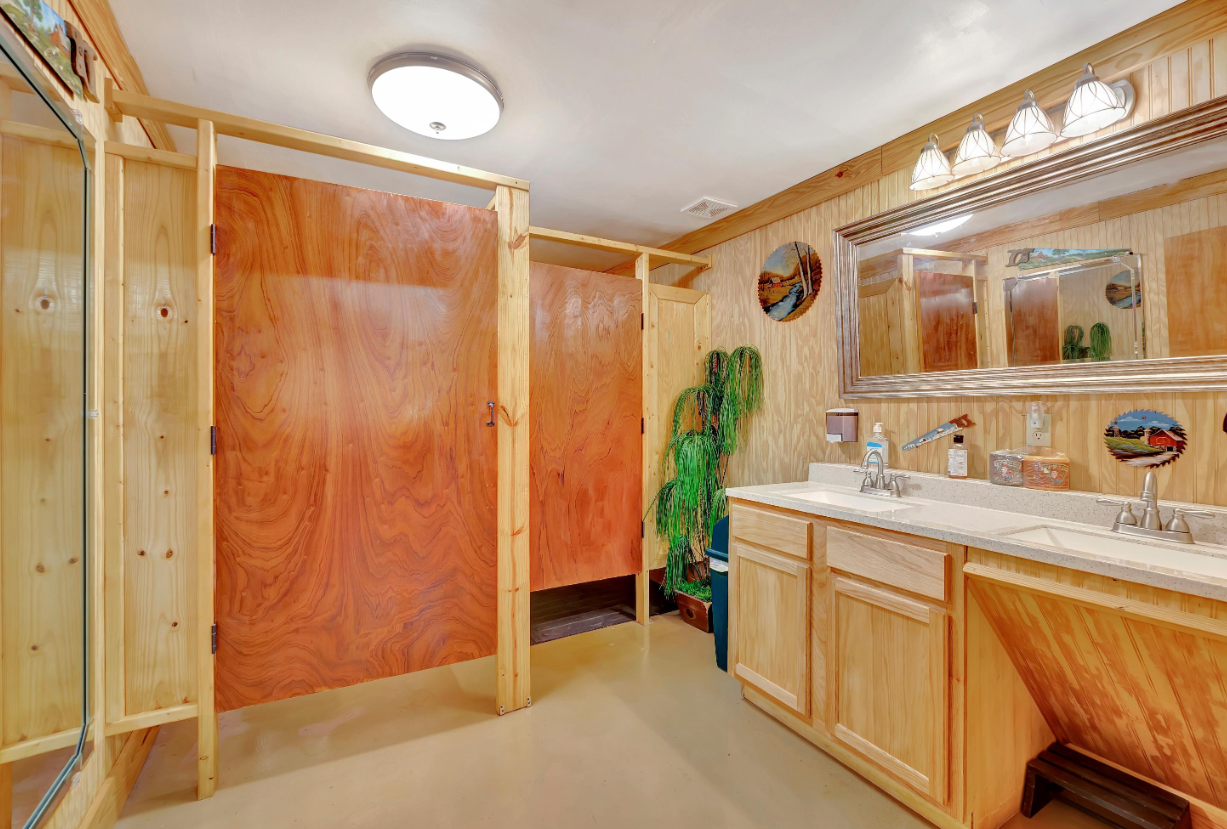 Wood-paneled bathroom with double sink vanity, large mirror, and tiled shower area