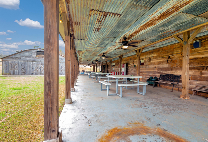 Rustic open-air pavilion with picnic tables and weathered metal roof beside a grassy field