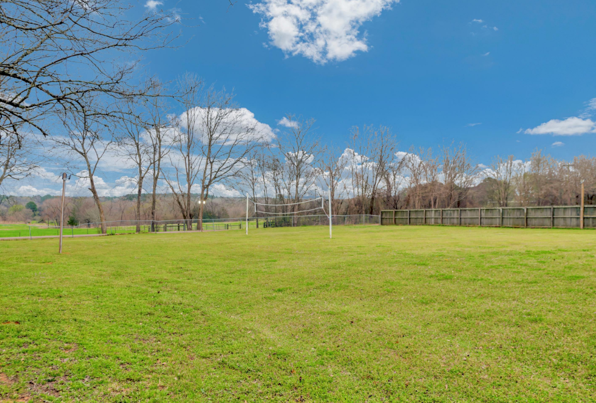 Wide grassy park field under a blue sky with clouds and leafless trees