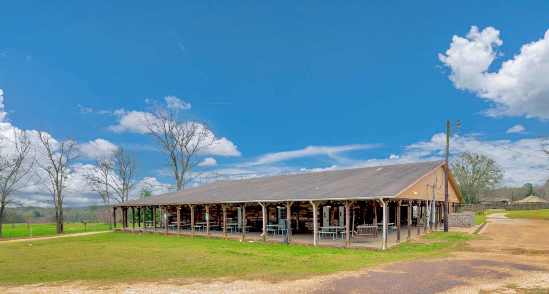 Rustic barn with a long metal roof in a grassy field under a bright blue sky with clouds
