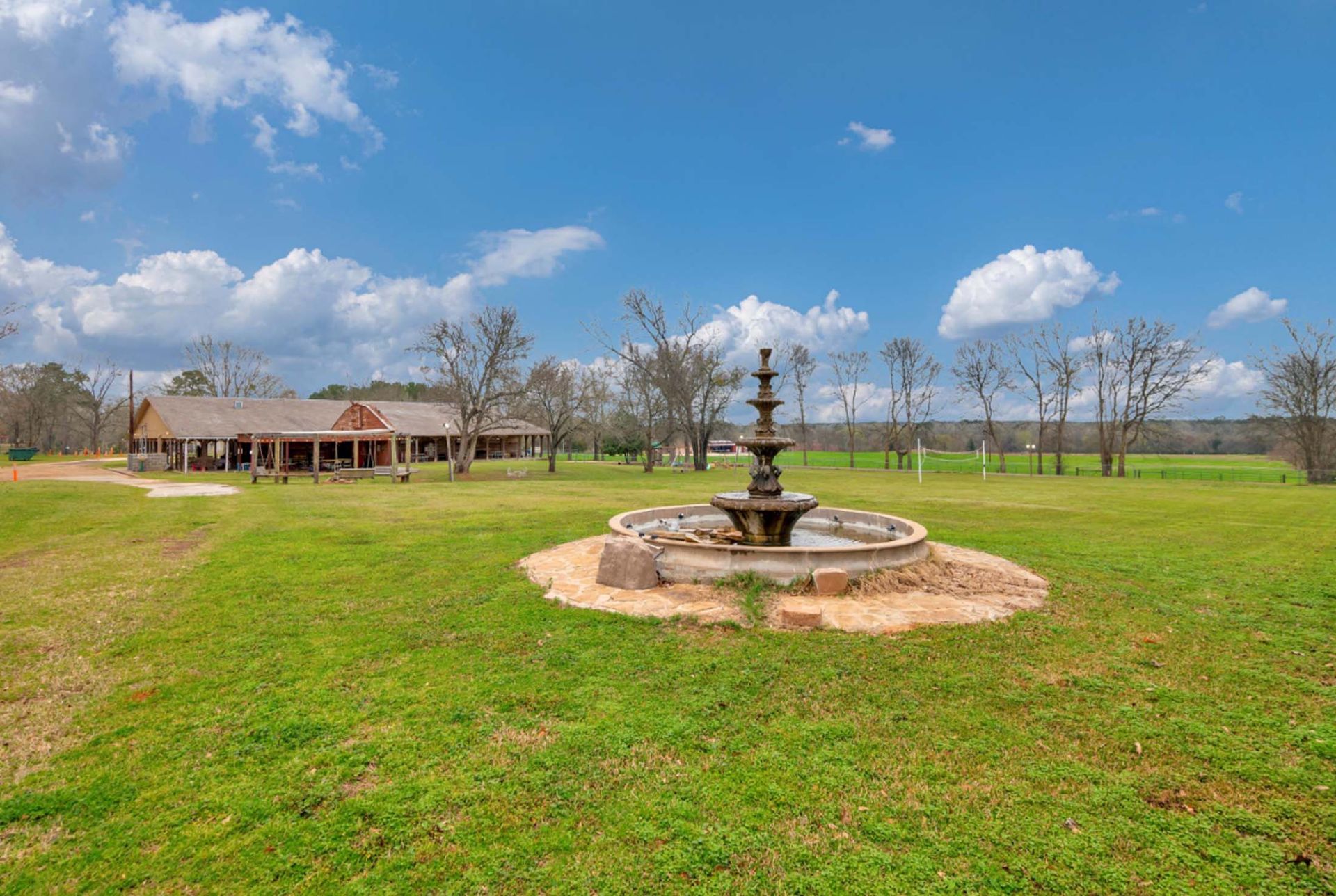Large grassy yard with a stone fountain in the center and a house under a blue sky in the background