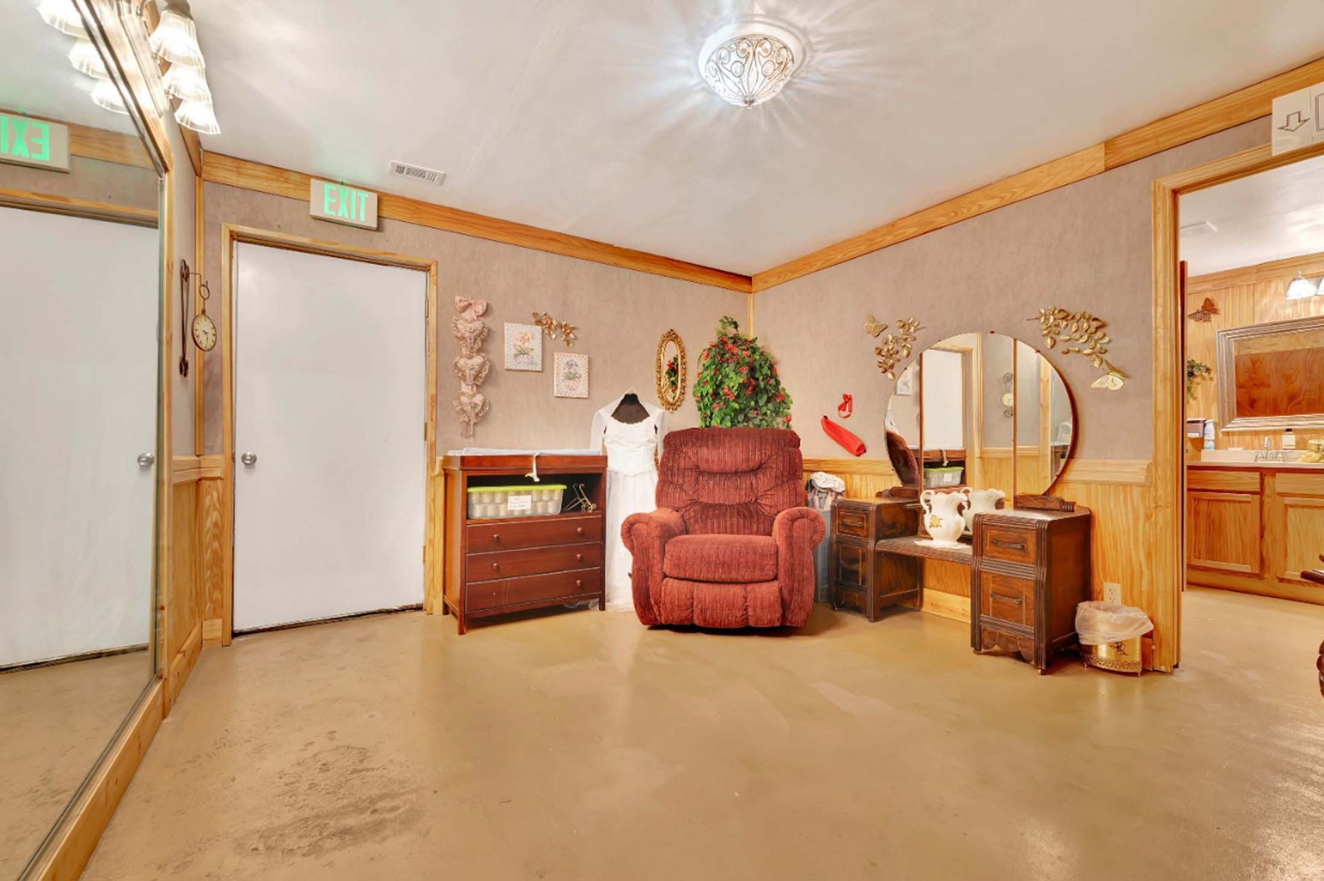 Empty room with beige walls, red recliner, dresser, mirror, and closed door under a ceiling light