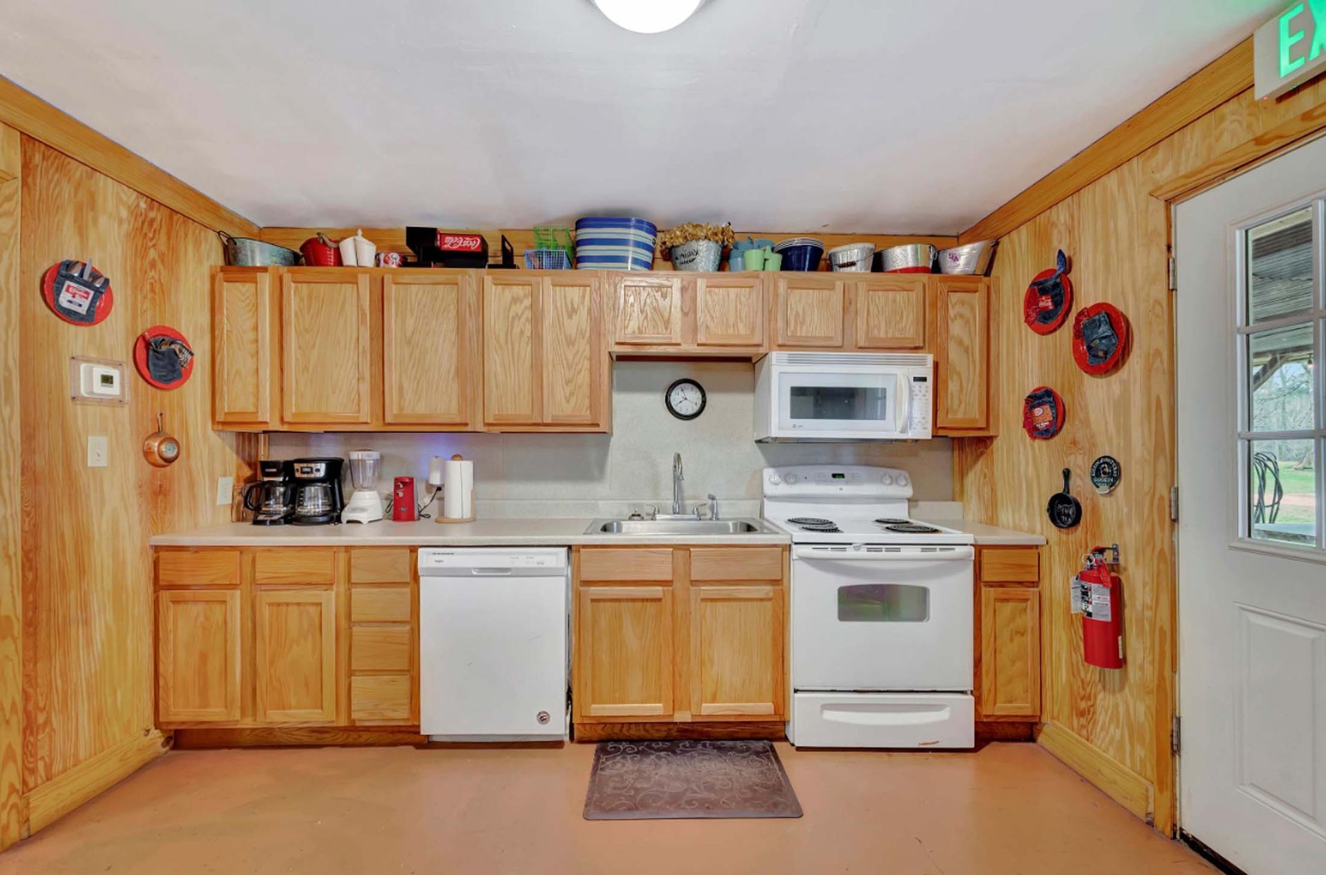 Small kitchen with wood cabinets, white appliances, a window, and decorative wall plates.