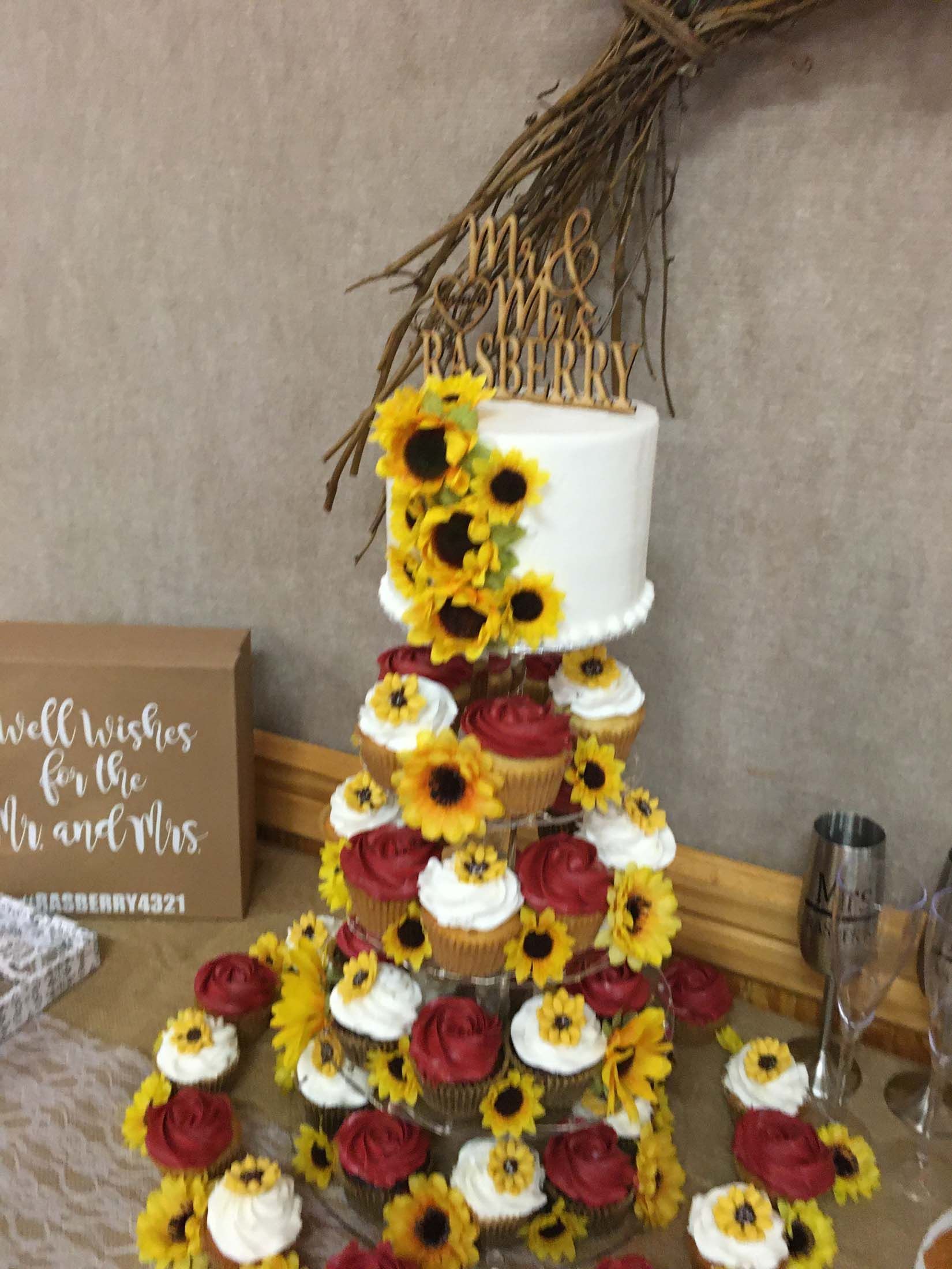 White tiered cake decorated with yellow, white, and red flowers on a table.