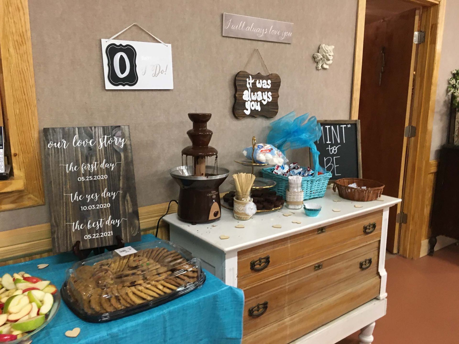 Dessert buffet with cake, fruit, drinks, and decorated chalkboard signs on a wooden sideboard
