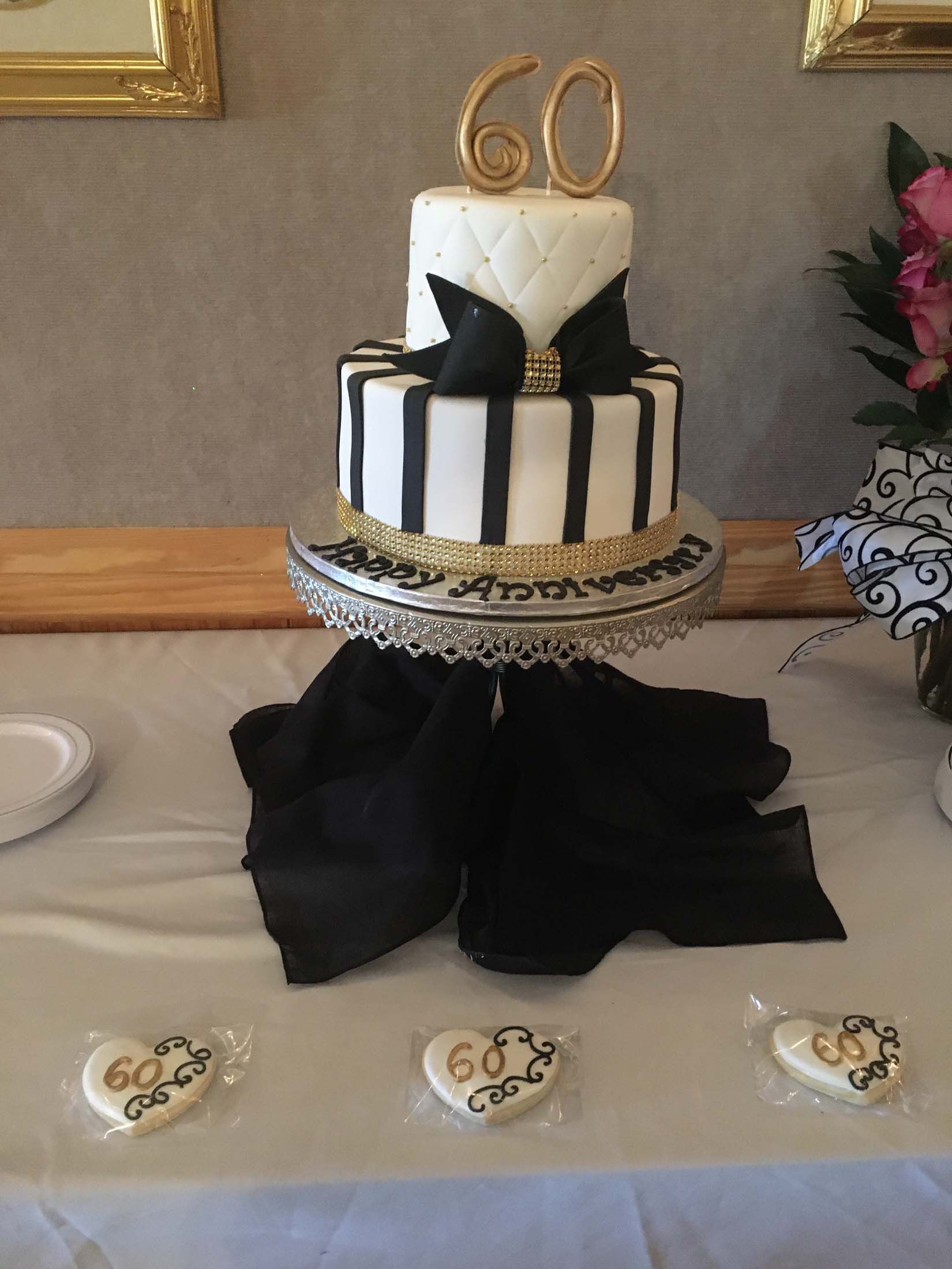 Black-and-gold 60th birthday cake on a decorated table with matching dessert cookies