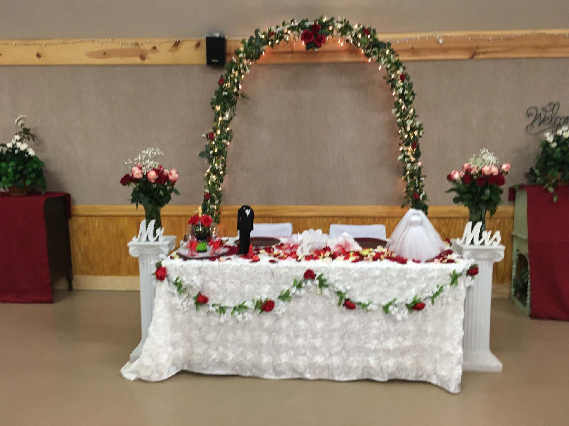 Decorated wedding reception table with floral arch, white tablecloth, and flower arrangements on either side