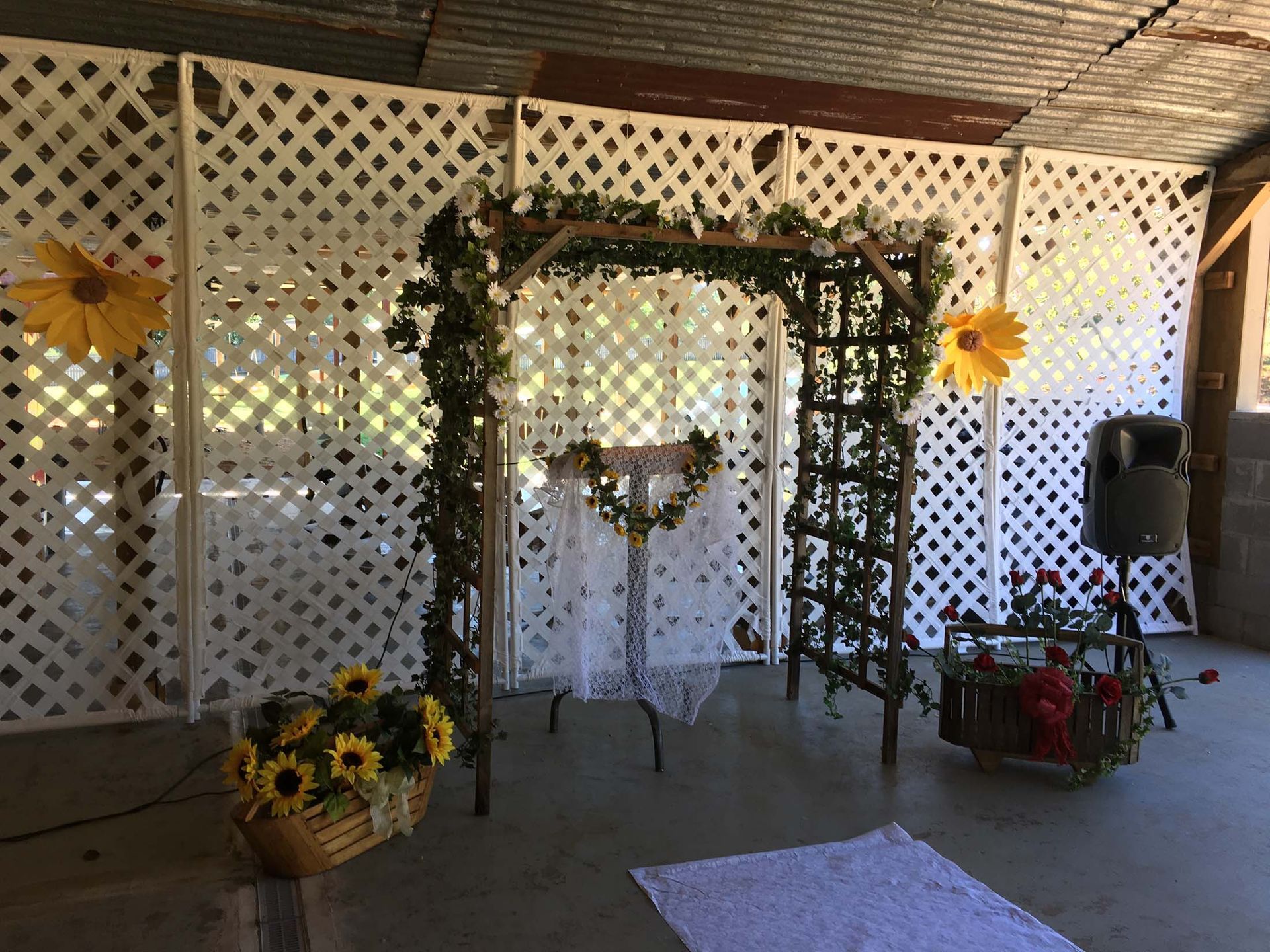 White lattice arch decorated with greenery and sunflowers at an outdoor event backdrop.