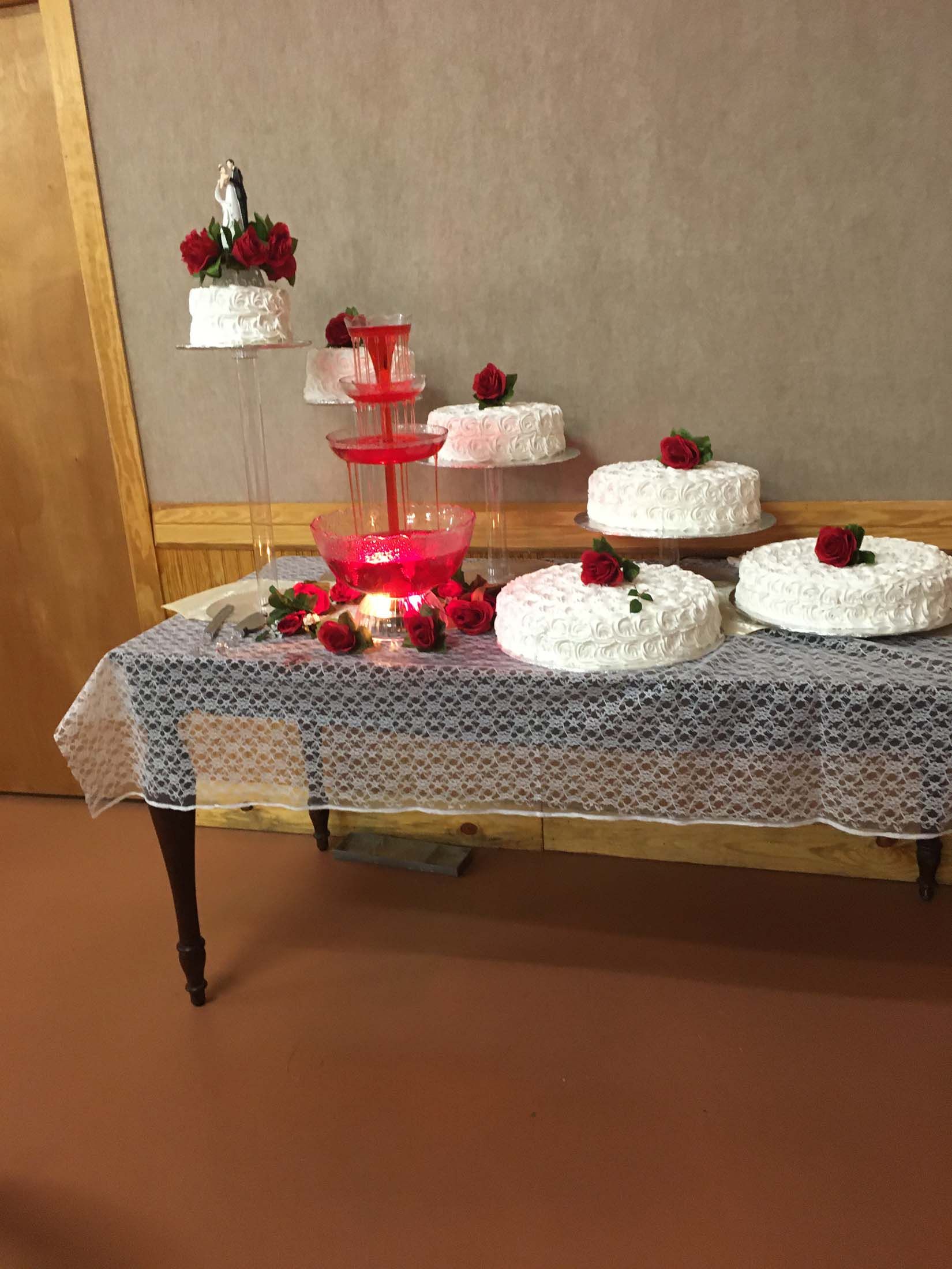 Decorated dessert table with white cakes, red flowers, and a red tiered stand on a lace tablecloth