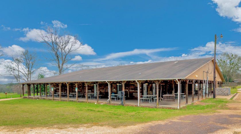 Large open-sided barn with a metal roof in a grassy rural field under a blue sky