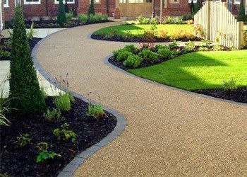 A resin bound walkway leading to a house with a lush green lawn. Installed by Essex Resin driveways