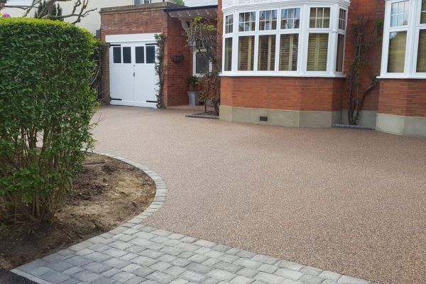 A brick house with a light coloured Resin driveway and a white garage door. Installed by Essex Resin driveways