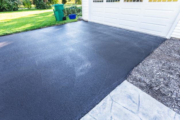 A black asphalt driveway next to a white garage door in Essex