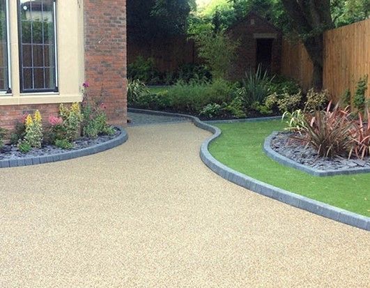 A resin bound driveway leading to a house with a brick wall and a fence. Installed by Essex Resin driveways