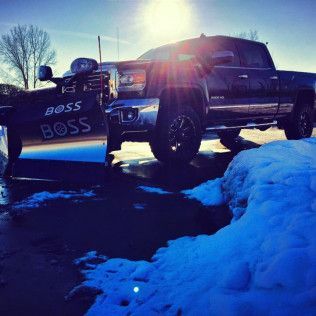Black pickup truck with a BOSS snowplow, parked on snow, sunny day.