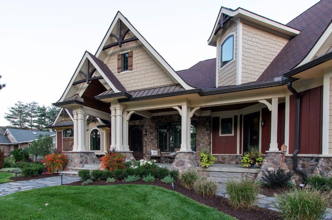 A house with a front porch, stone and tan exterior, and a red roof with manicured landscaping.