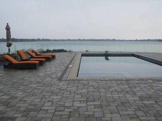 Poolside scene with lounge chairs, umbrella, and a body of water under an overcast sky.