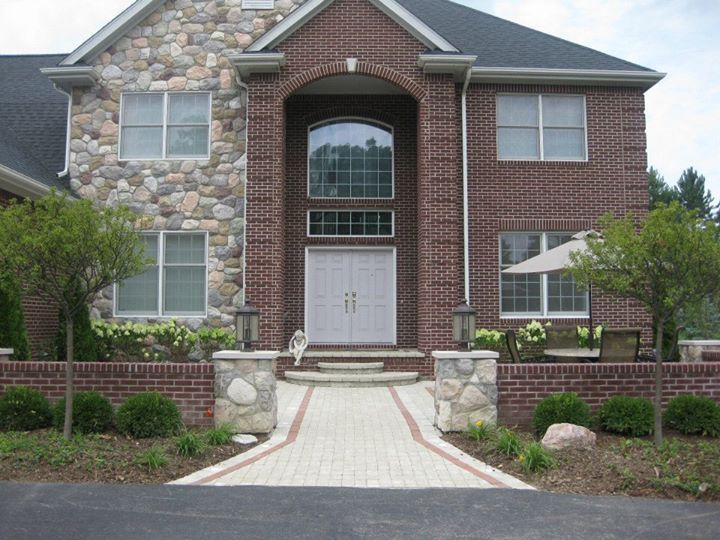 Brick and stone two-story house with a paved walkway leading to the front door.