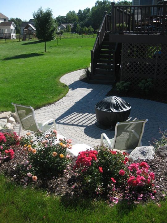 Backyard patio with fire pit, chairs, and colorful rose bushes. Path leads to a wooden deck.