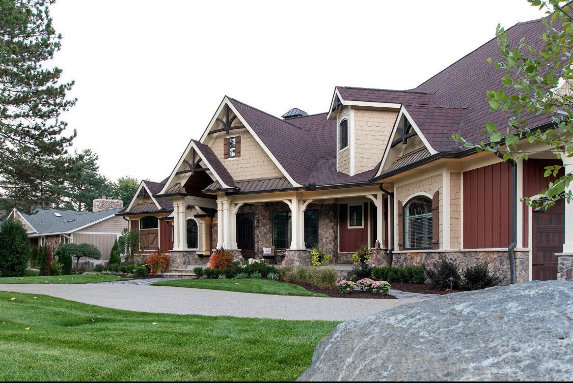 Tan and red craftsman-style house with stone accents, a covered porch, and a gravel driveway.