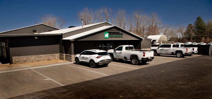 Exterior view of a commercial building with vehicles parked in front. Dark gray siding, blue sky.