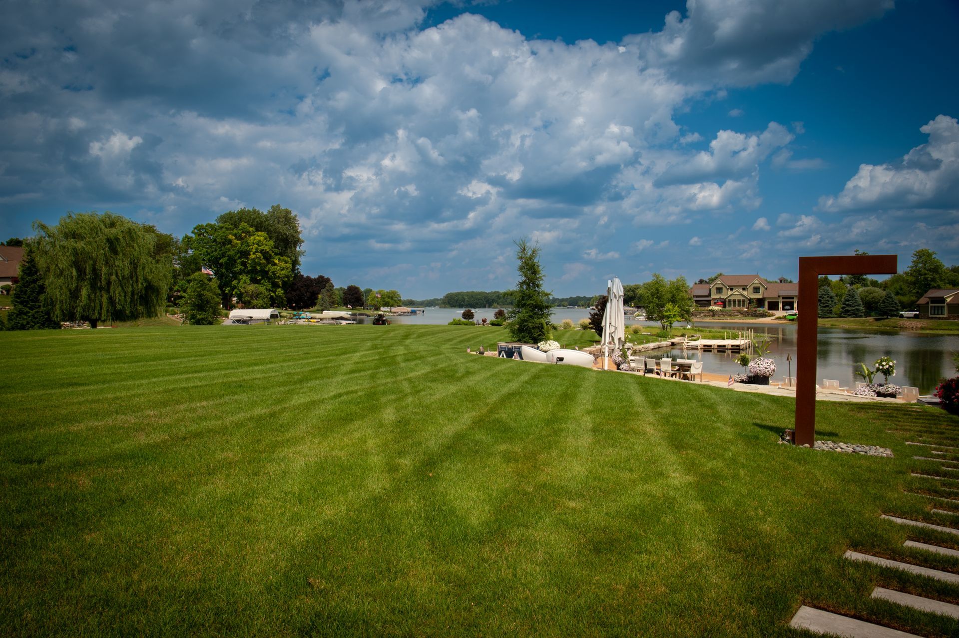 Lush green lawn slopes to a waterfront with a bright blue sky and fluffy white clouds.