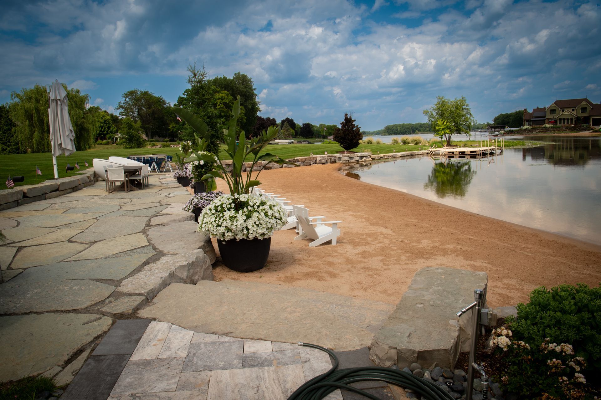 Patio by a sandy beach with potted flowers and water view.